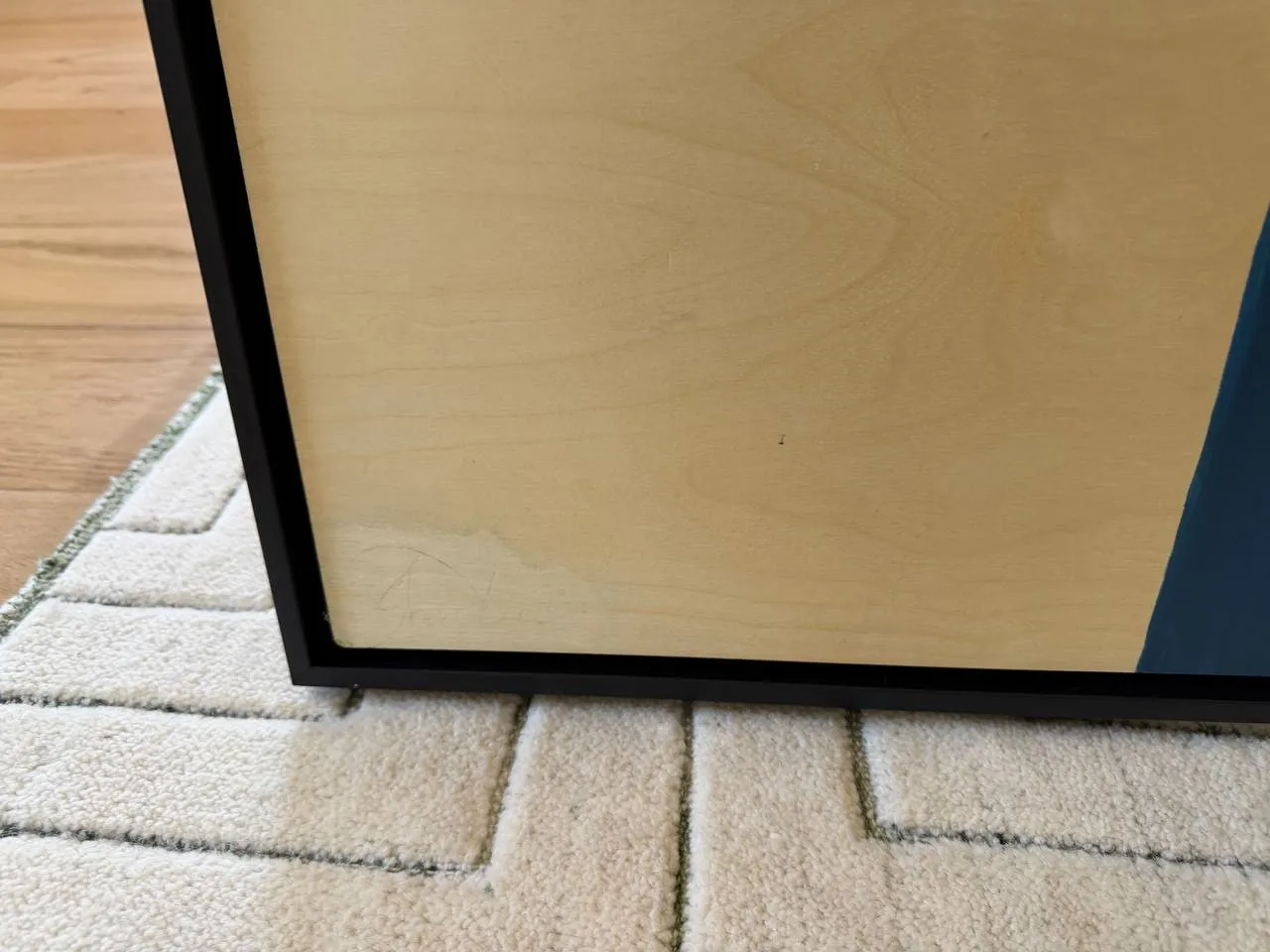 Detail of the lower-left corner: the bare birch-wood ground and the black floater frame, with the faint pencil signature