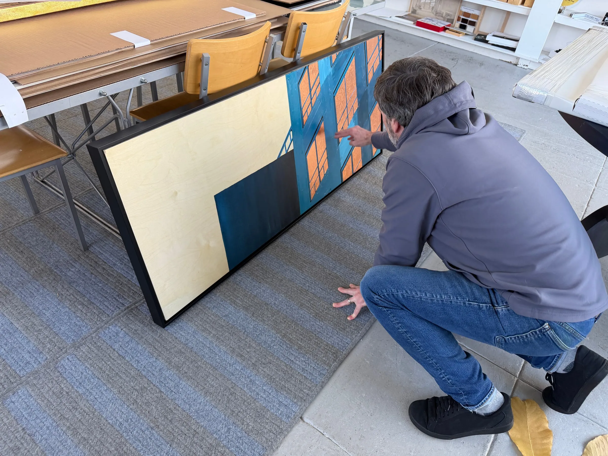 The print in a black floater frame, leaning against a work table at the framer, being inspected