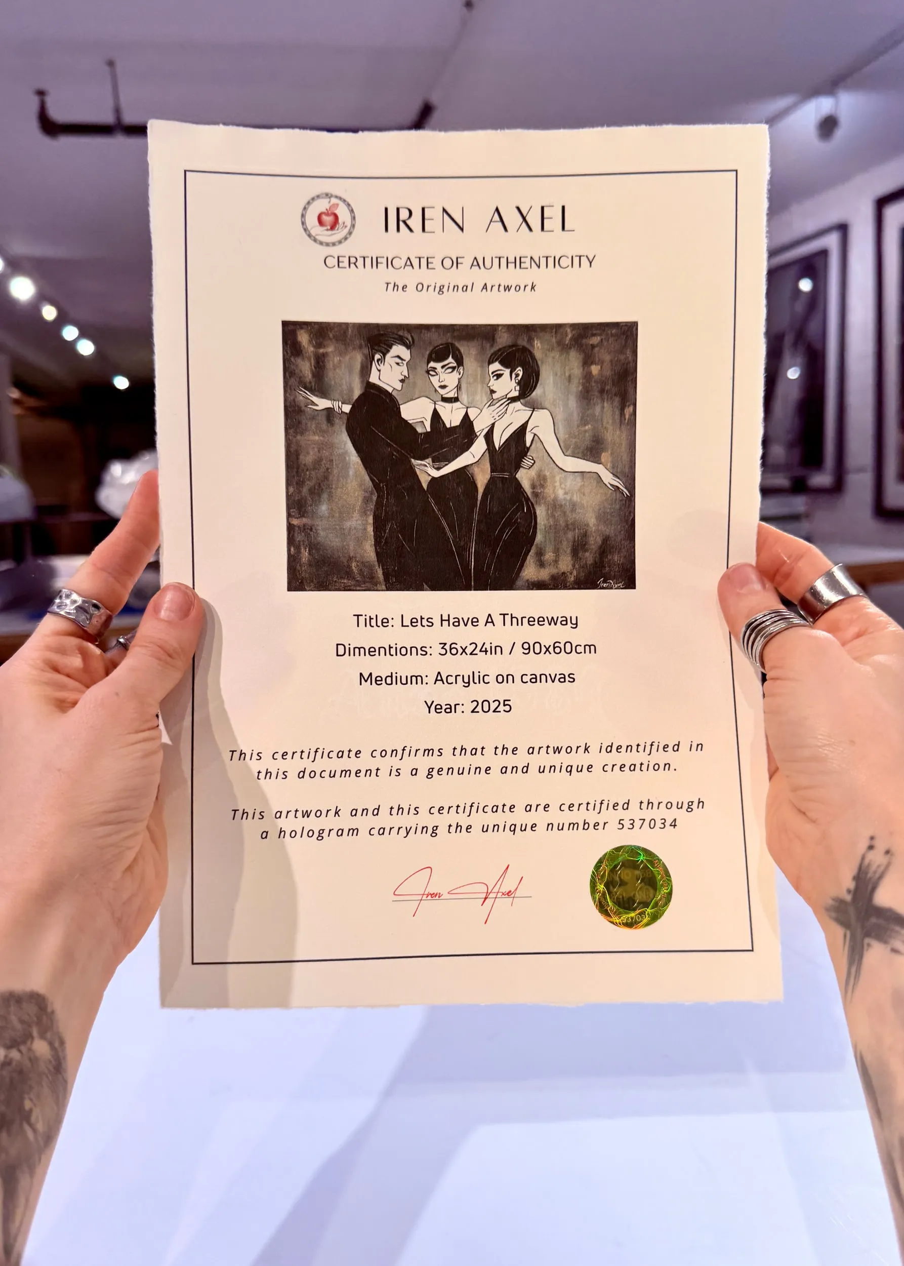 The signed certificate of authenticity for Let's Have A Threeway, hologram number 537034, held up in the gallery
