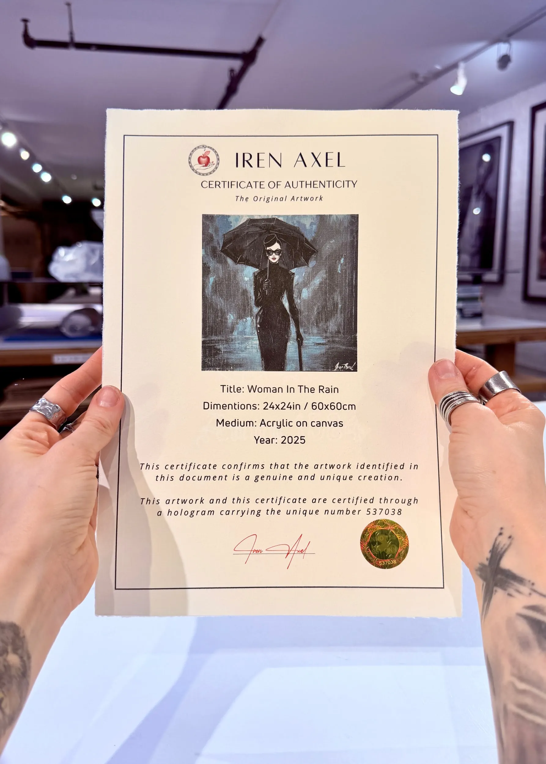 The signed certificate of authenticity for Woman In The Rain, hologram number 537038, held up in the gallery