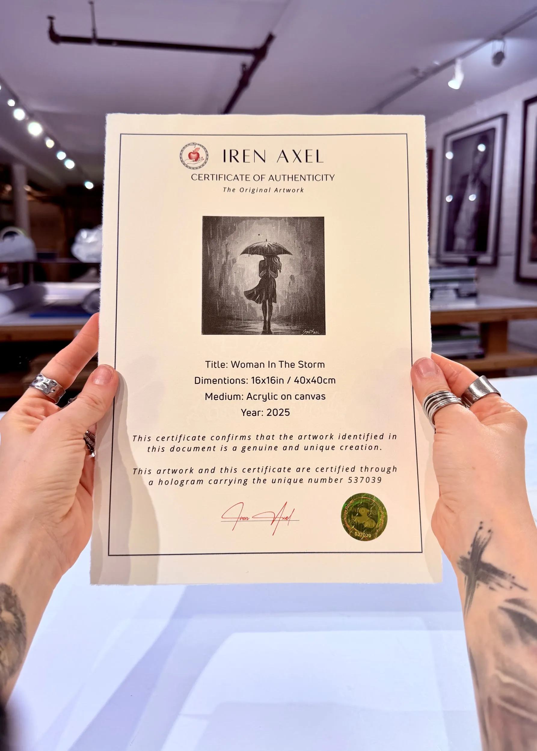 The signed certificate of authenticity for Woman In The Storm, hologram number 537039, held up in the gallery